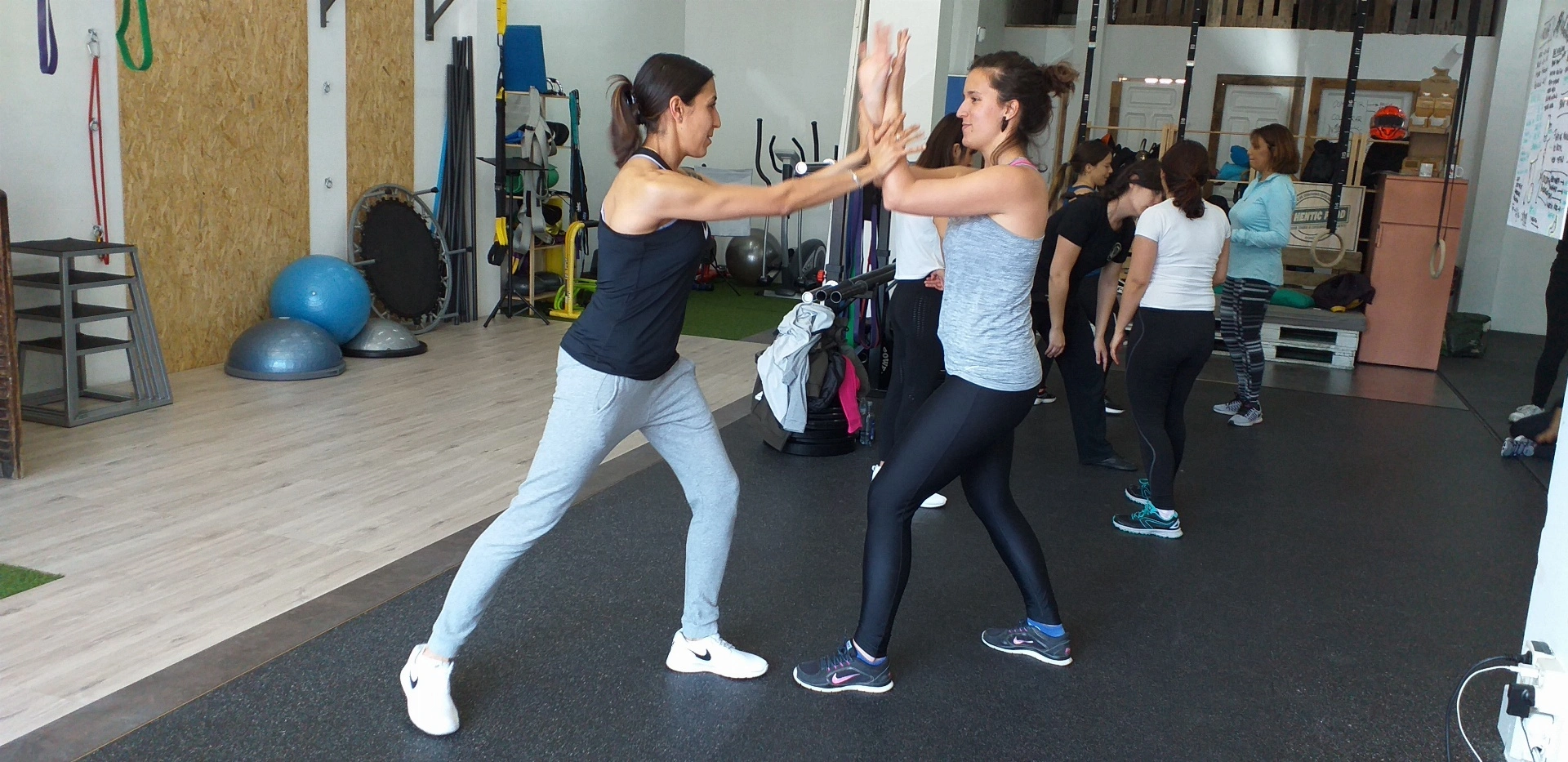 Dos mujeres practicando movimientos de defensa personal en un gimnasio.